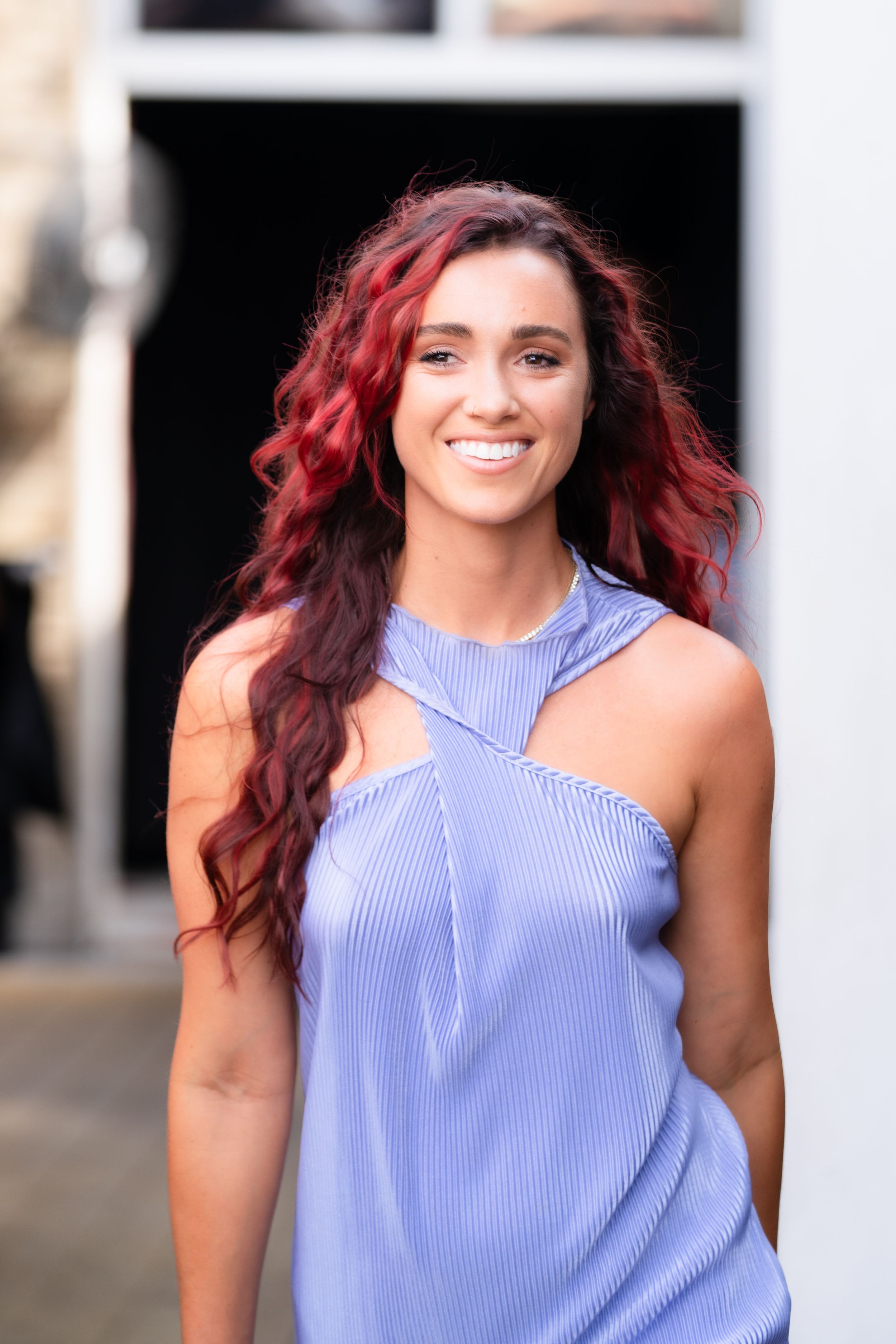 Woman wearing blue striped halter top smiles while posing outdoors with red-tinted hair.