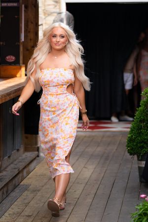 Woman in floral print summer dress with cutouts walks along wooden deck wearing platform sandals.