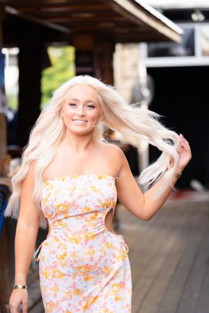 Woman in floral dress with blonde hair dancing and twirling outdoors in summer.