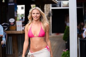 A woman in a pink bikini walking along a beachside boardwalk on a sunny day.