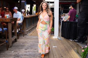 Woman in floral summer dress walking on rustic wooden boardwalk under shade.
