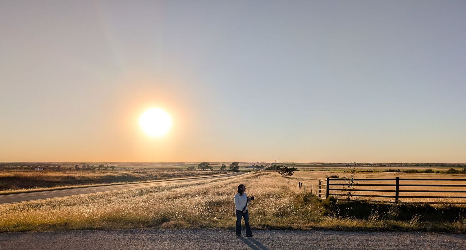 Panoramic sunset view over a vast open field with a fence silhouette.