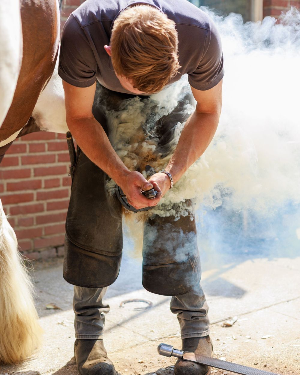 Craftsperson in black shirt working with flour and dough on a rustic wooden surface creating clouds of white powder.