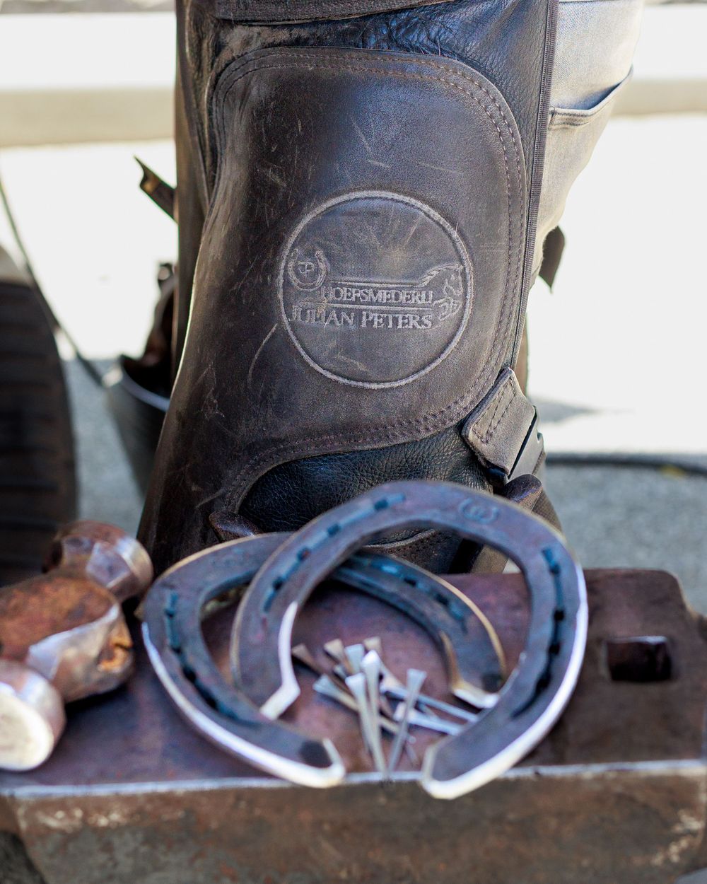 Close-up view of leather boots and horseshoes on a wooden surface showing equestrian equipment details.