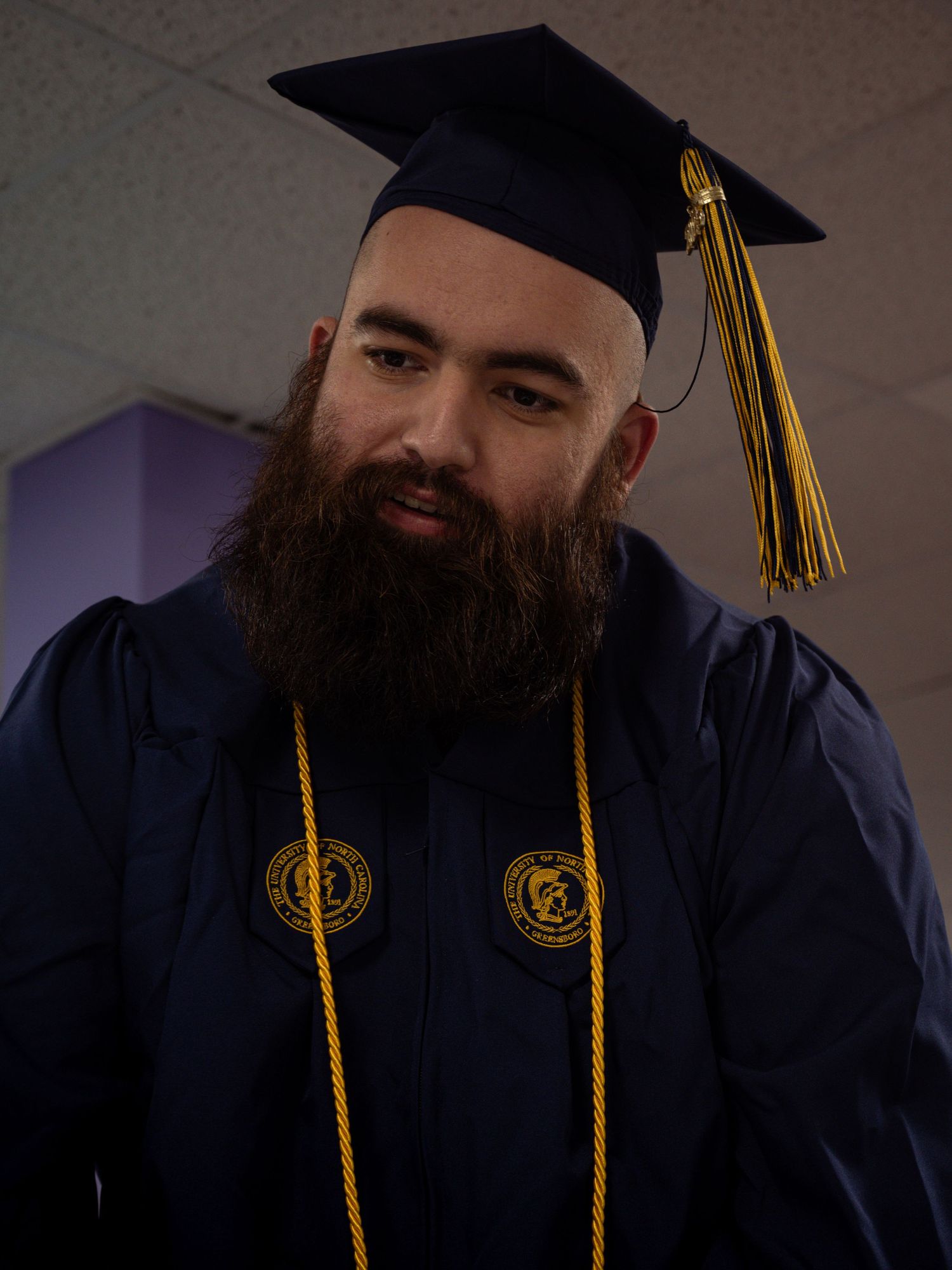 Graduate in navy blue cap and gown with gold tassel and honor cords in formal portrait.