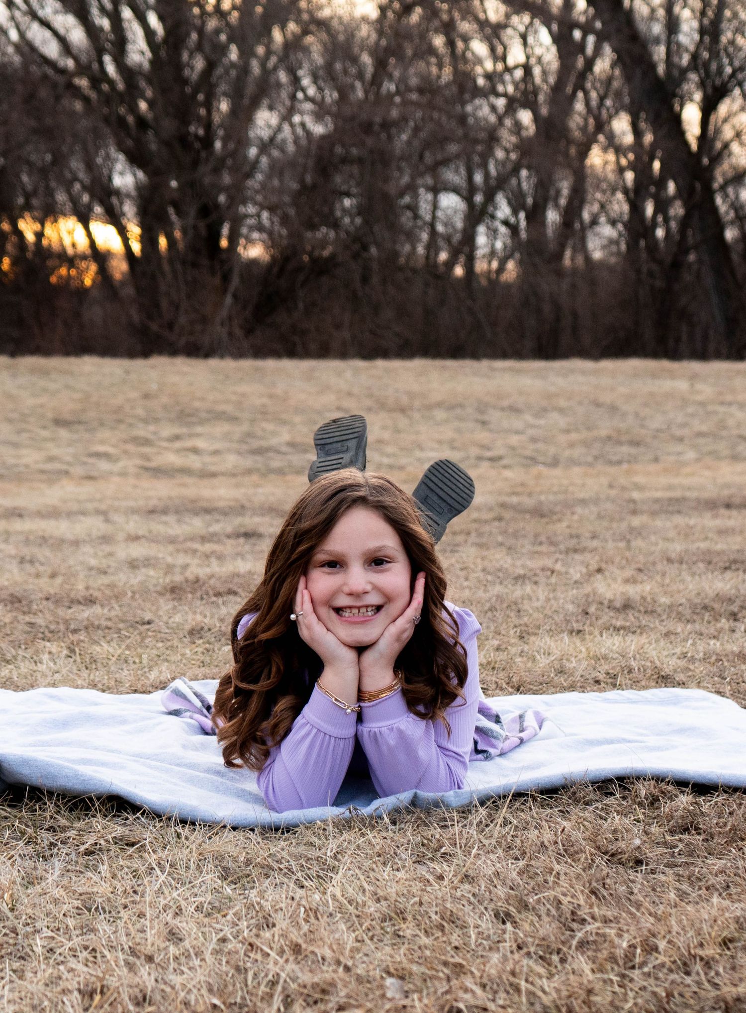 Smiling girl lying on blanket in field at sunset with boots up.