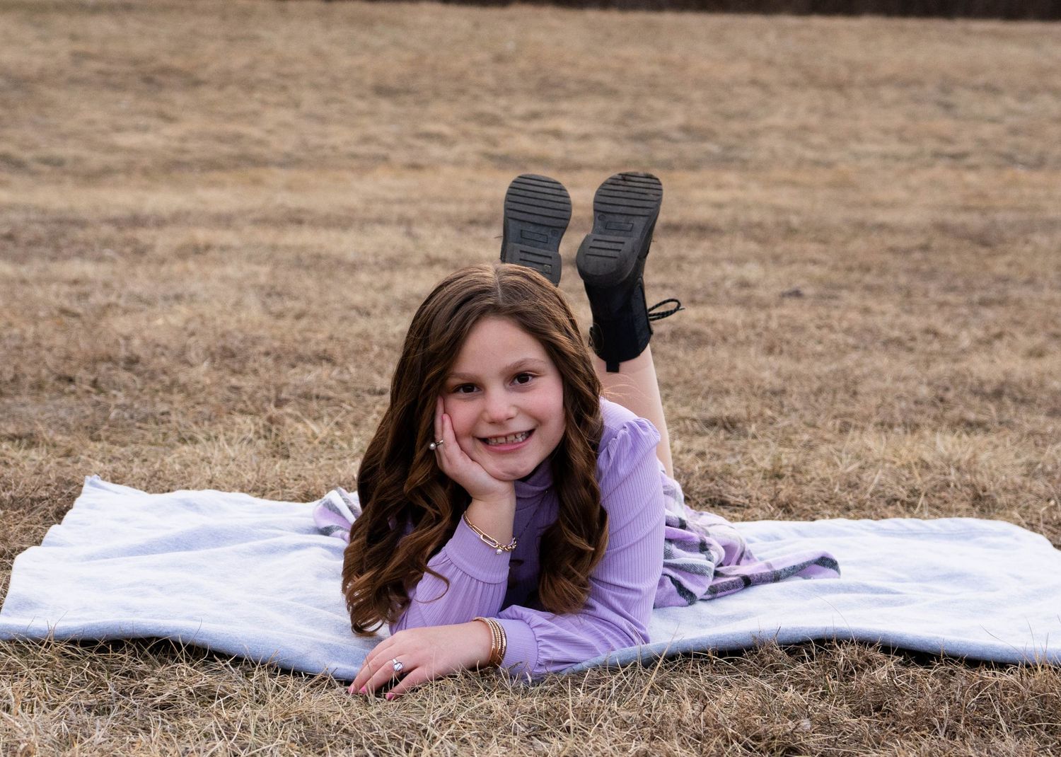 Happy girl lying on blanket in dry grass field smiling at camera.