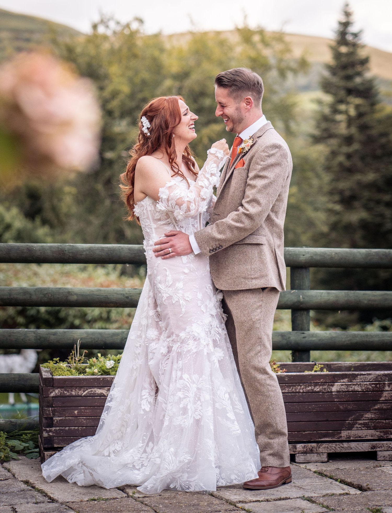 A couple in wedding attire share a romantic moment on a rustic wooden bridge surrounded by autumn foliage.