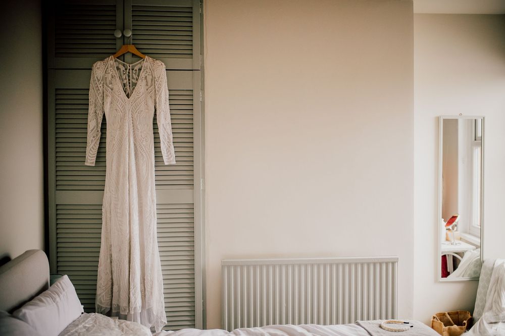 A series of white wedding dresses and bridal gowns displayed against a neutral wall with shutters.