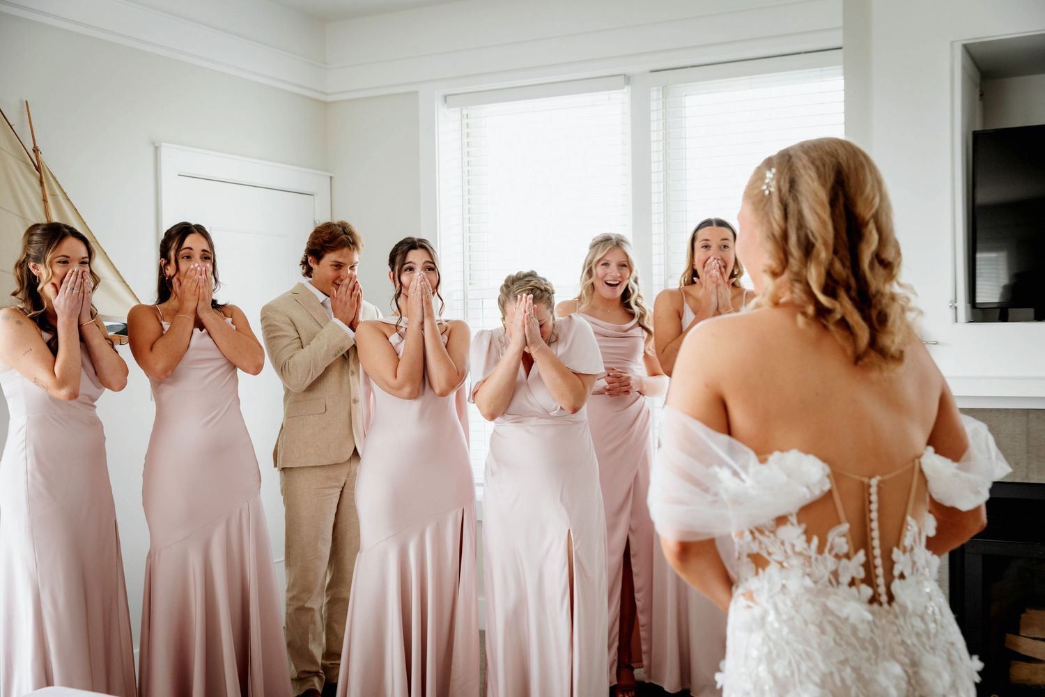 A series of bridesmaids in blush pink dresses react emotionally during a wedding day bride's first look in upscale hotel room in Bay Harbor.