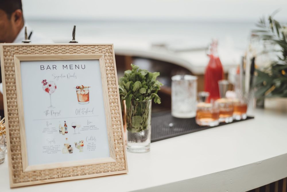 Elegant wedding reception details featuring framed bar menus and decorative elements on a white tablecloth.