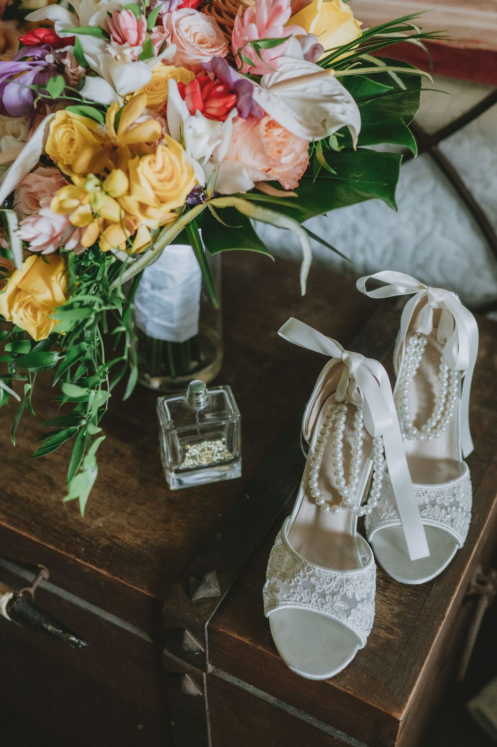 Elegant white bridal shoes with floral decorations and wedding bouquets displayed on a rustic wooden surface.