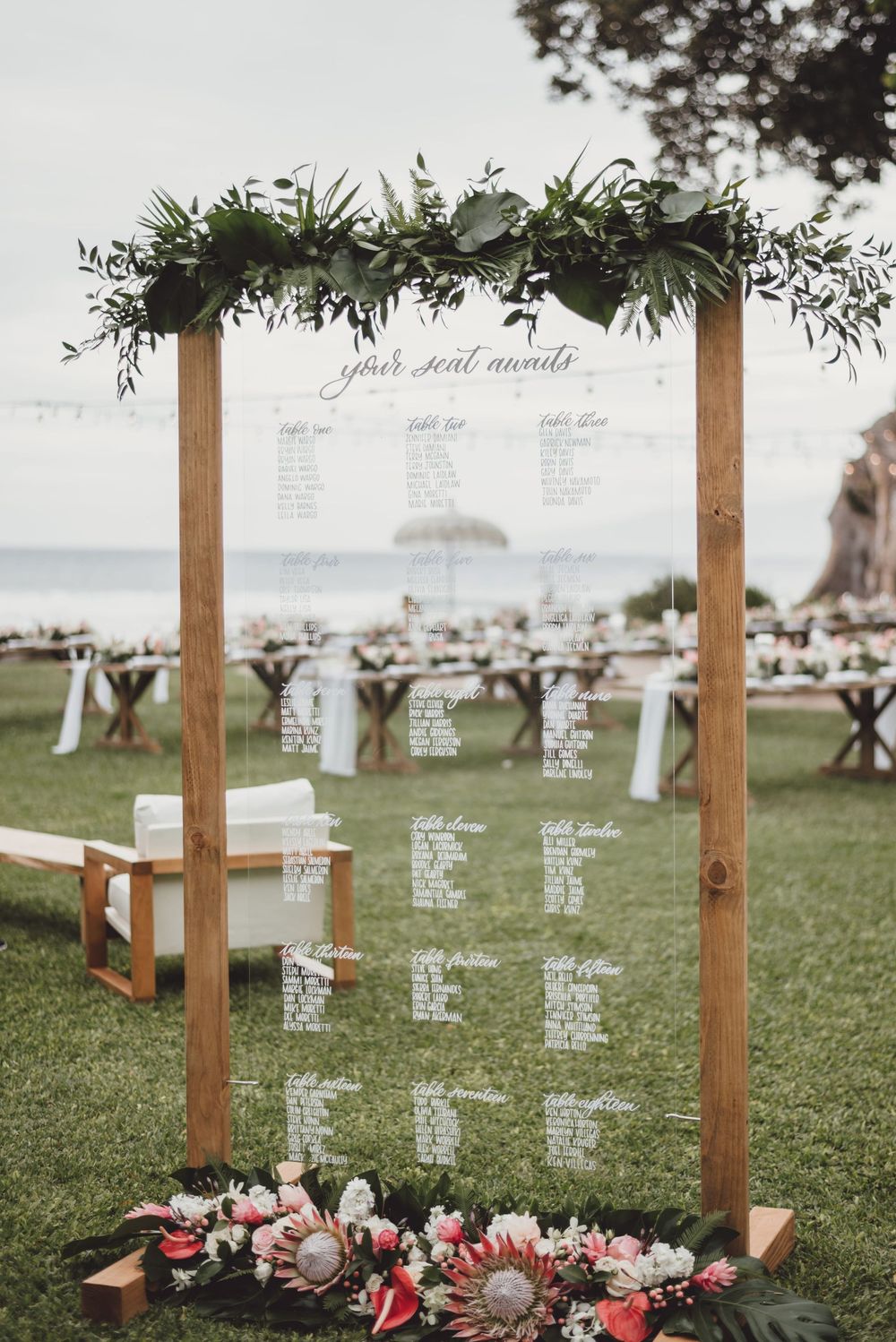 Wooden posts with seating charts and floral arrangements create an elegant outdoor wedding display on a grassy lawn.