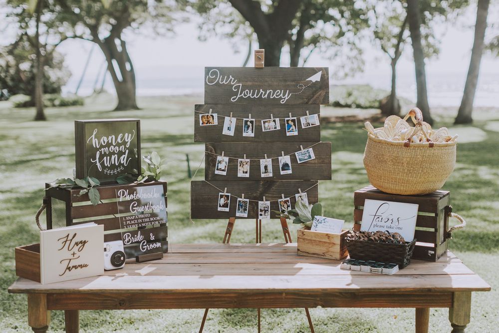 Rustic outdoor wedding guest book table with vintage decor, wooden signs and photo display under a tree.