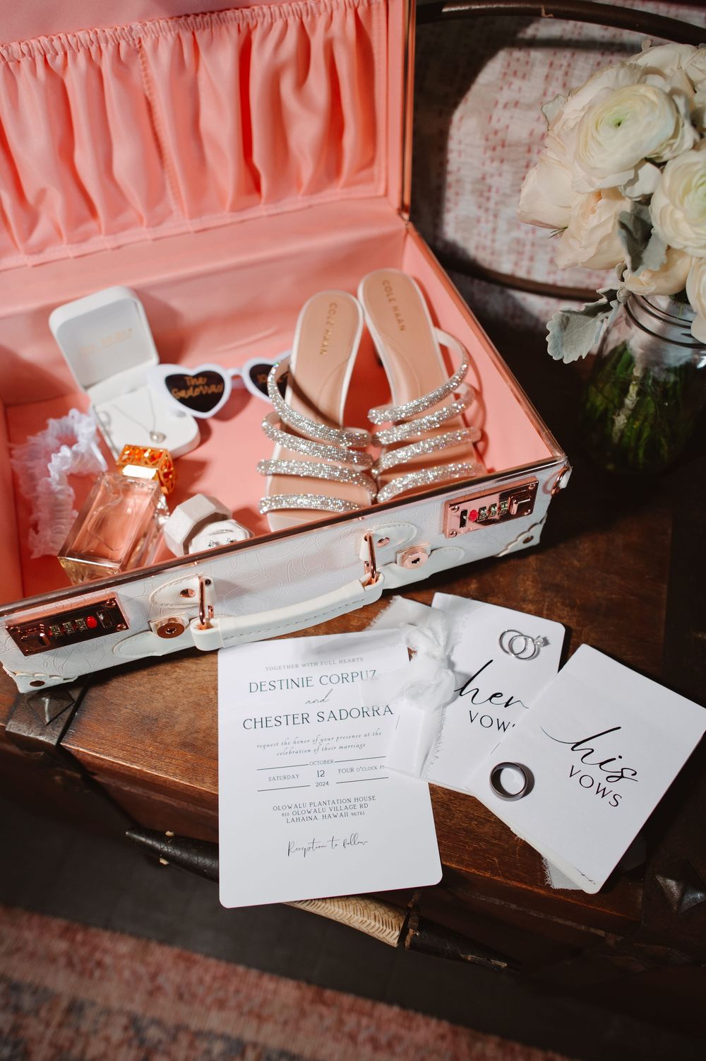 Wedding accessories including sparkly heels, sunglasses and invitation cards arranged in a pink-lined vintage suitcase.