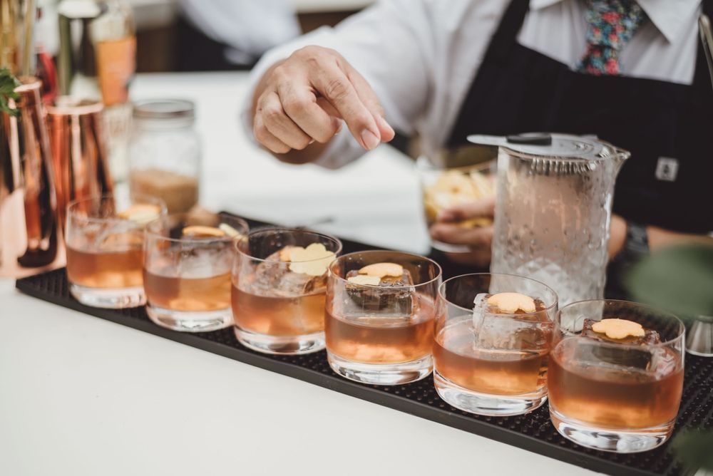 Several glasses of bourbon cocktails with ice cubes line up on a wooden bar counter during a tasting event.
