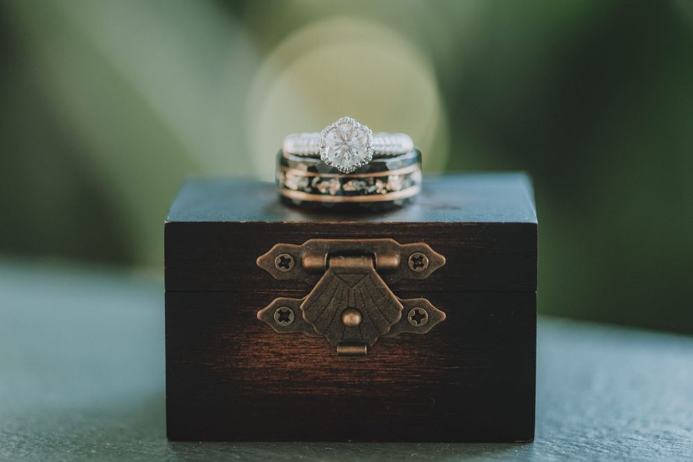 A vintage wooden jewelry box with ornate metal details sits on a blurred green background.