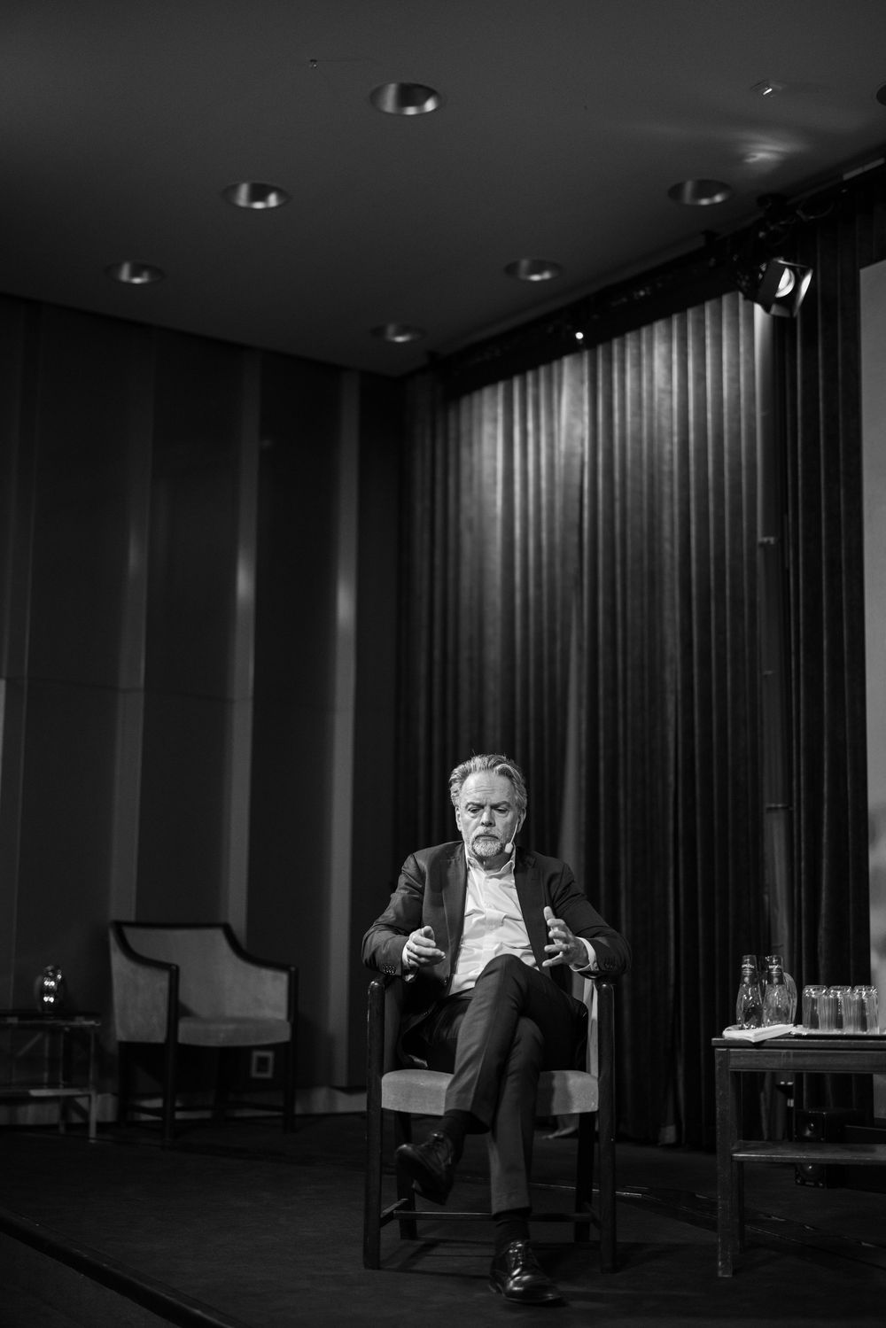 A black and white photo series showing someone seated in a dimly lit room with dark curtains and recessed lighting.
