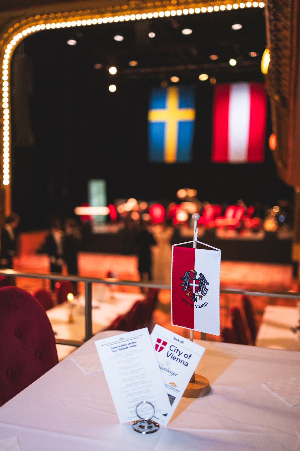 A series of small flags and table cards displayed at a formal event venue with decorative lighting in the background.