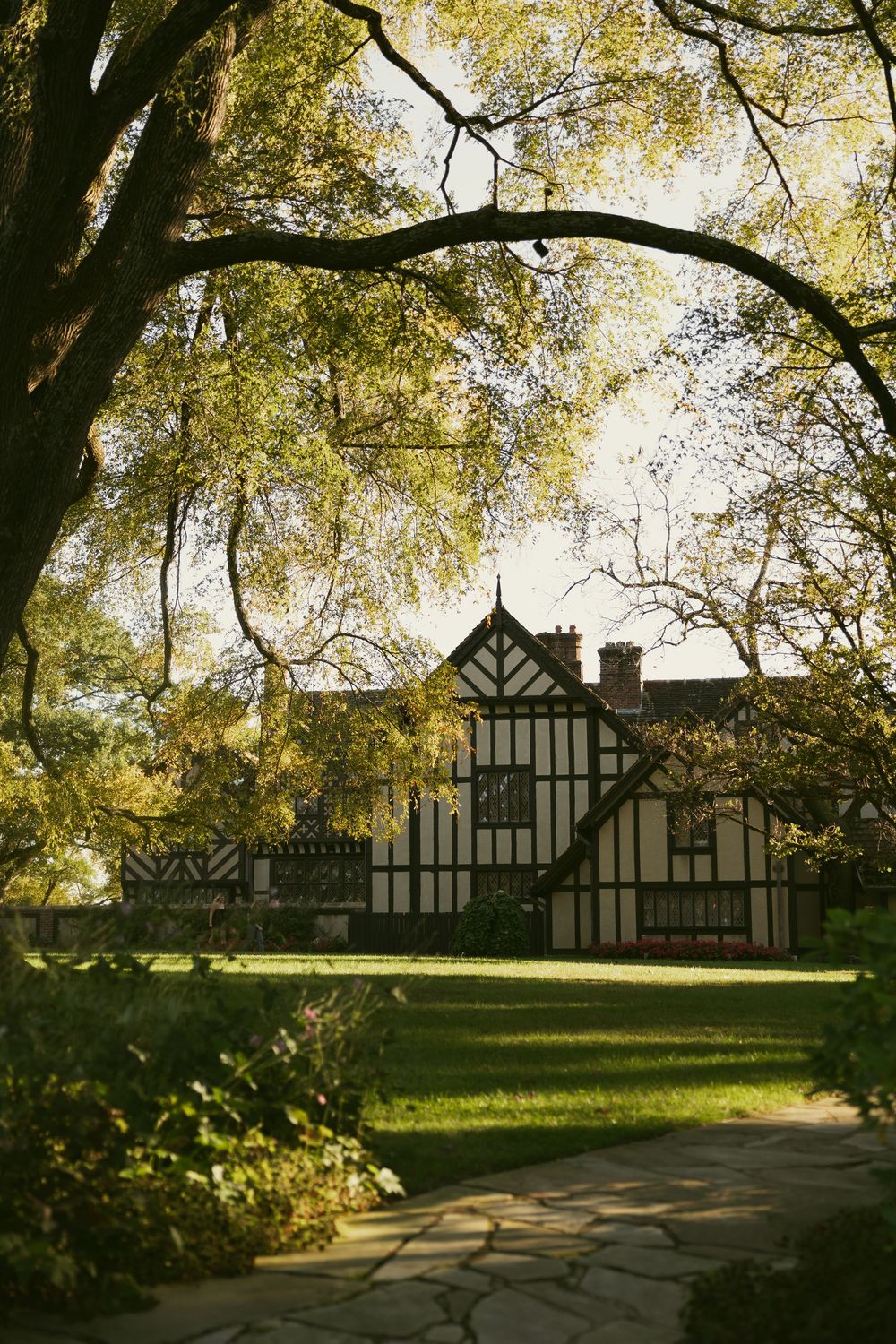 Tudor-style mansion with black and white timber framing set against trees in golden sunlight.
