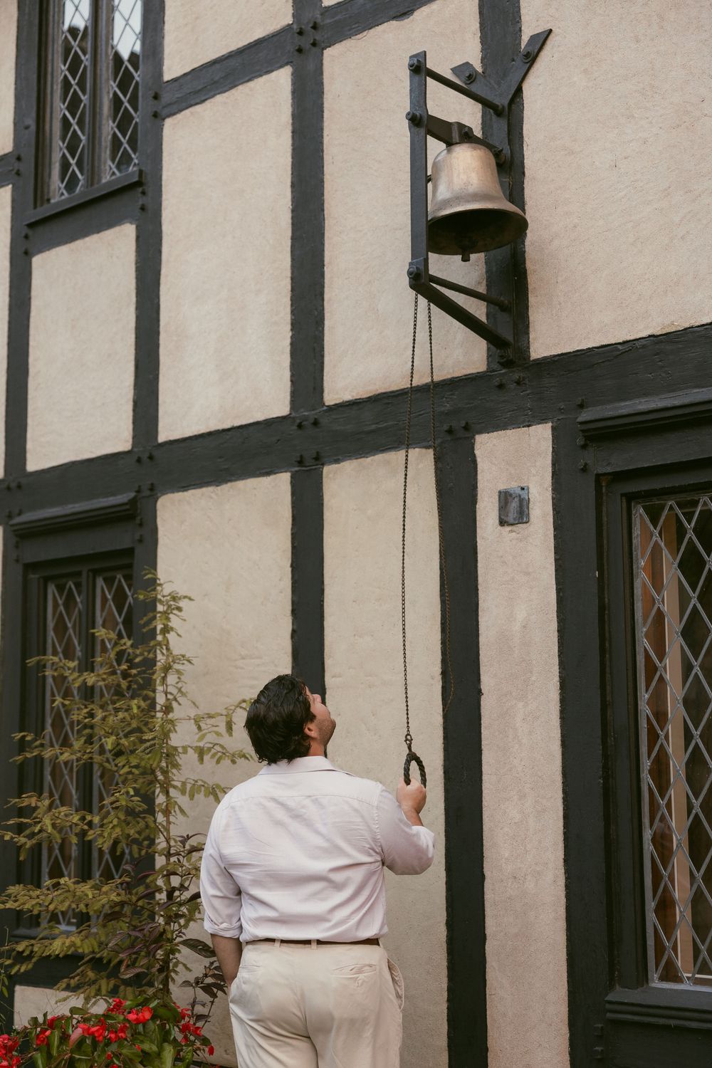 Person in white clothing hanging decorations on a Tudor-style building exterior.