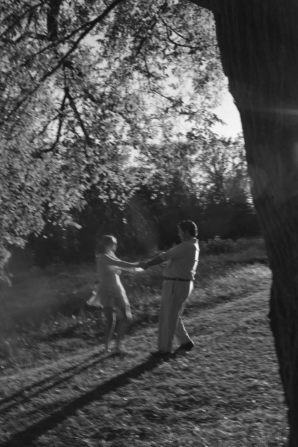 A black and white photograph shows two figures dancing together in a sunlit backyard of Agecroft Hall in Richmond, VA