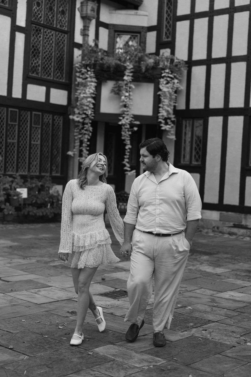 A couple holding hands while walking during their engagement session at Agecroft Hall in Richmond, VA in black and white