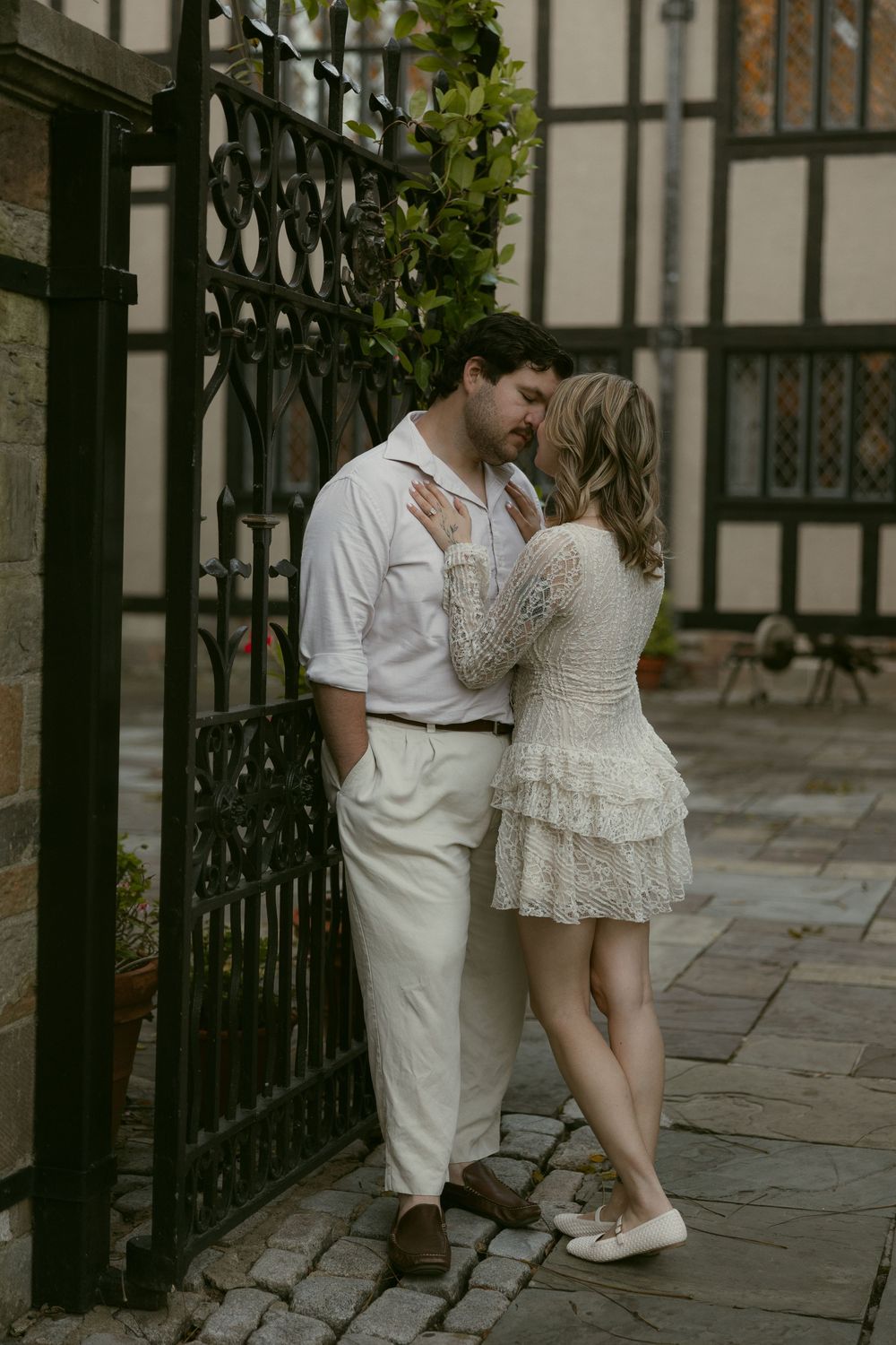 A romantic couple in white clothing shares tender moments by an ornate iron gate.