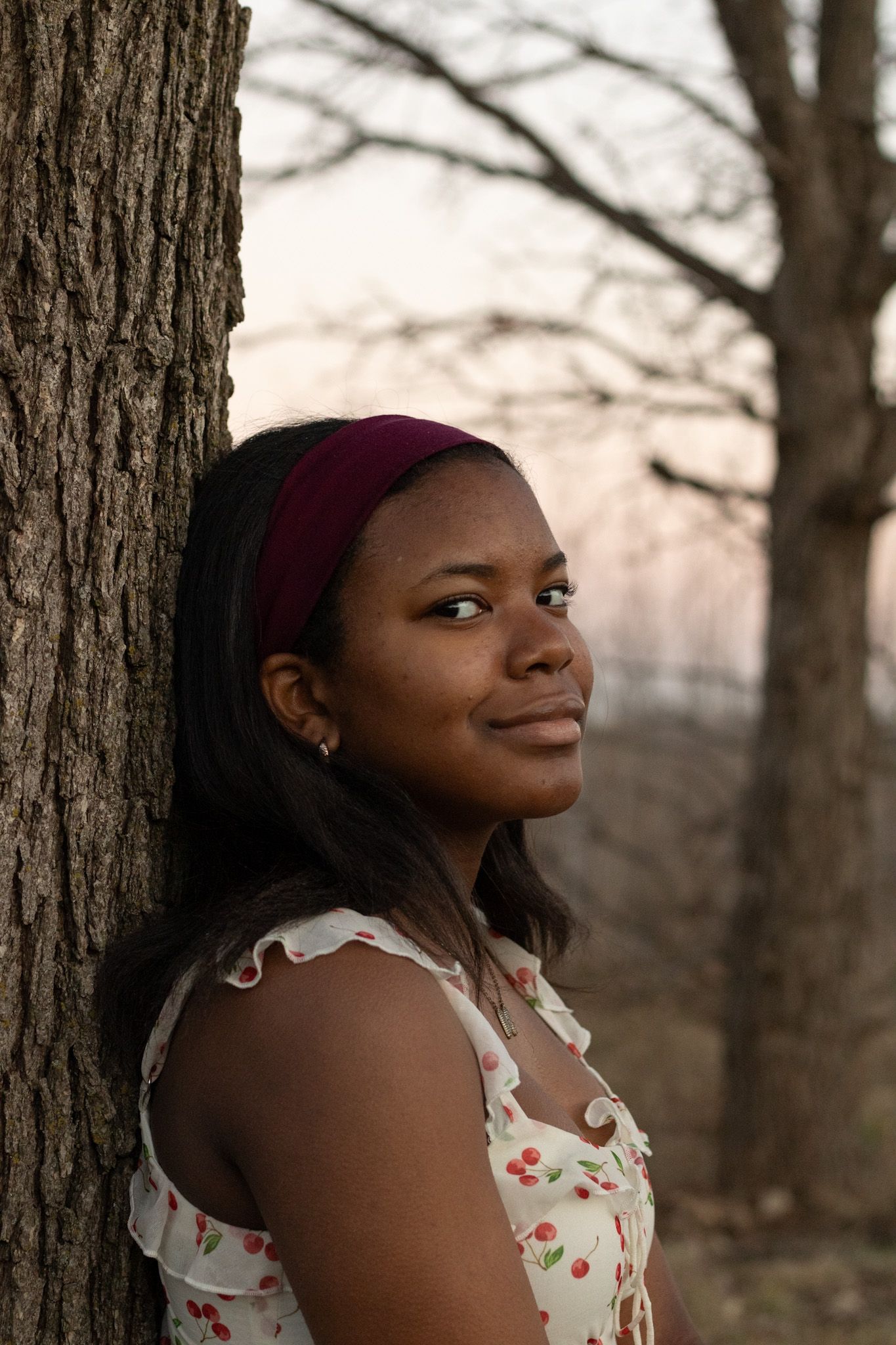 Portrait in a forest setting wearing a floral dress and burgundy headband.