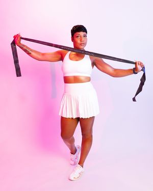 Person in white dress stretches with resistance band against pink background during fitness workout.