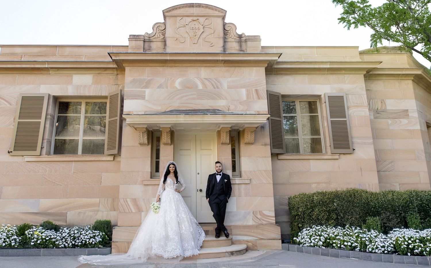 Elegant bride and groom pose on steps of a grand sandstone heritage building on their wedding day.