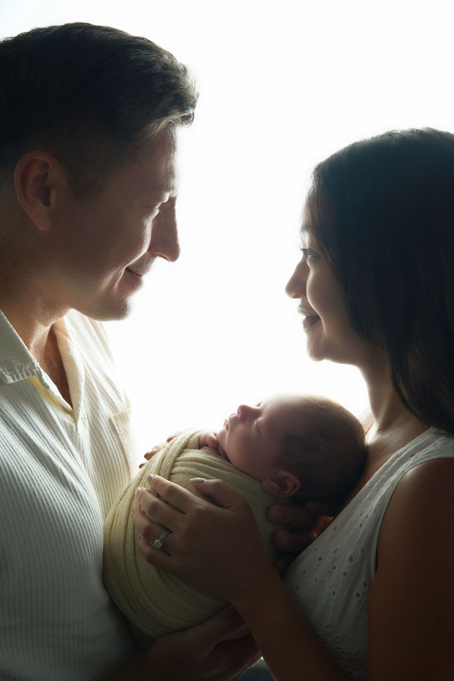 Silhouetted family portrait with baby in backlit window setting.