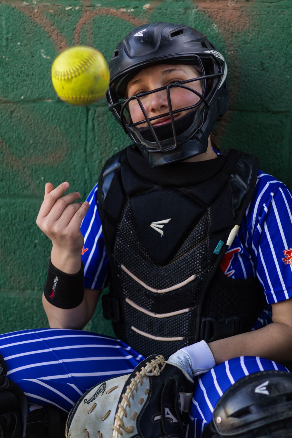 Action sequence of softball catcher in protective gear tracking yellow ball.