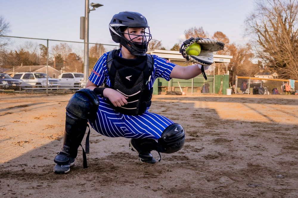 Softball player demonstrating fielding positions in blue striped uniform on dirt field.