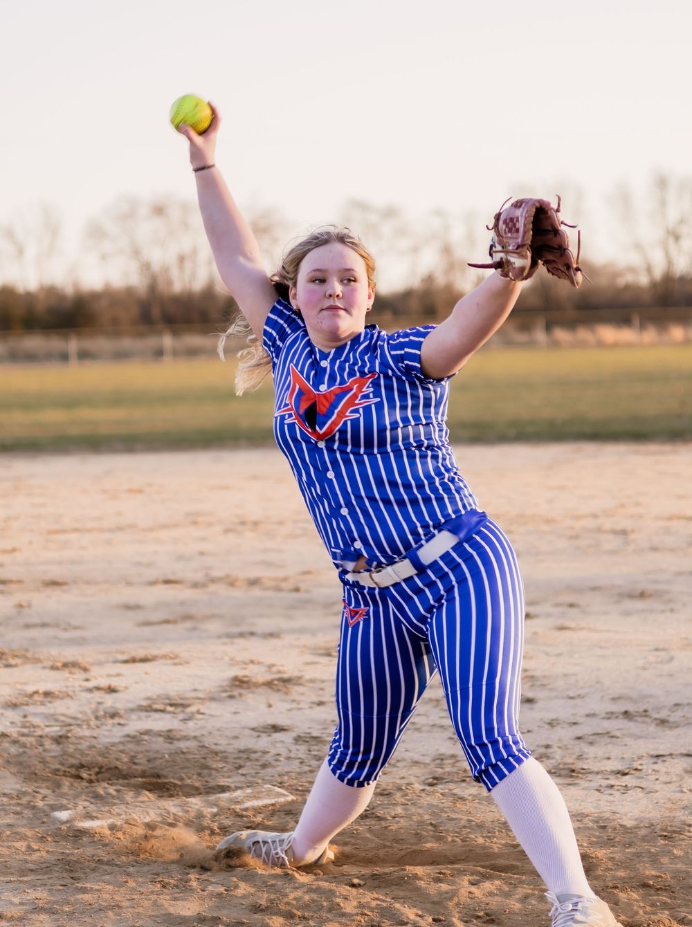 Dynamic sequence of softball pitching motions on dirt field at sunset.