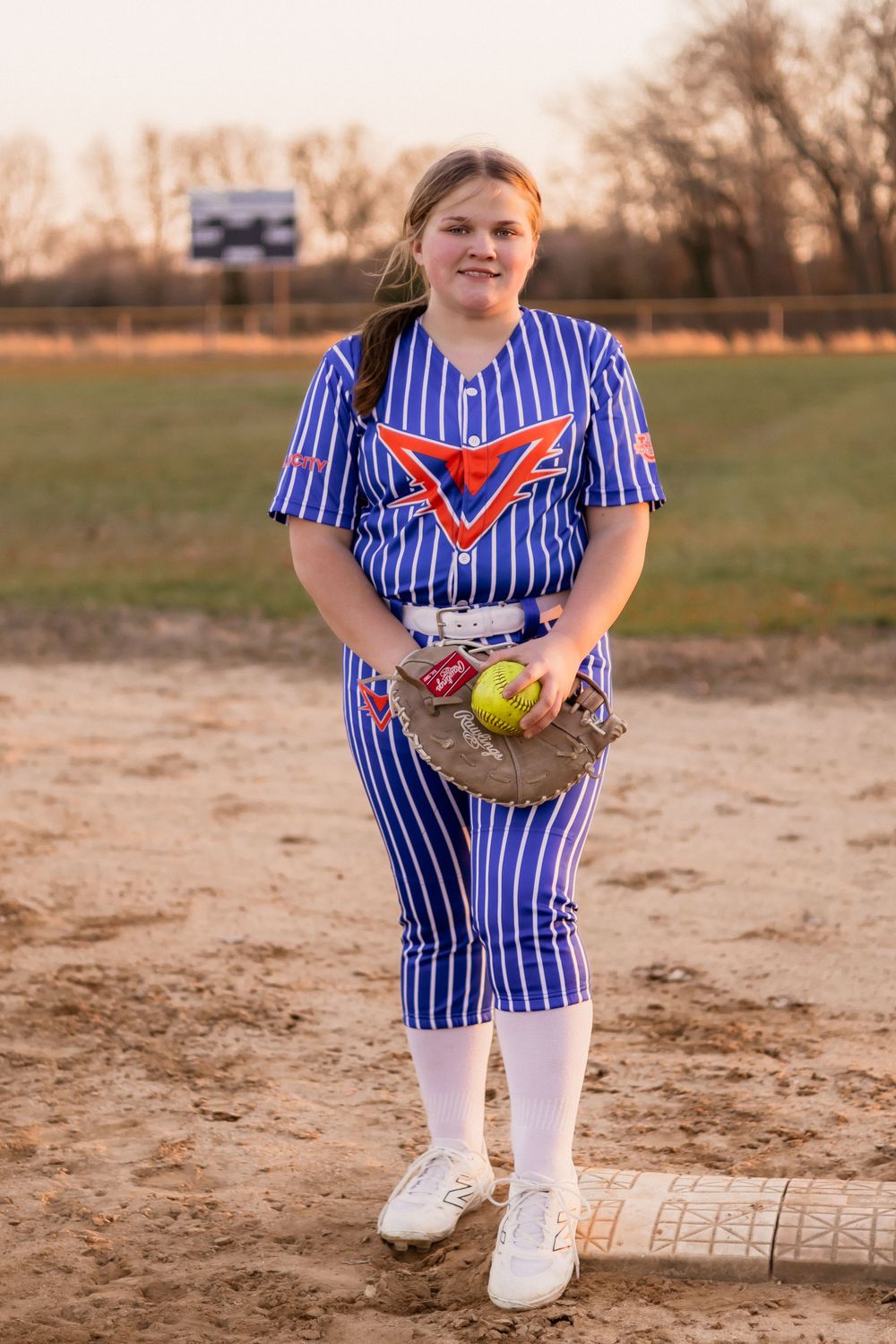 Softball player in blue striped uniform posing with glove and ball on field.
