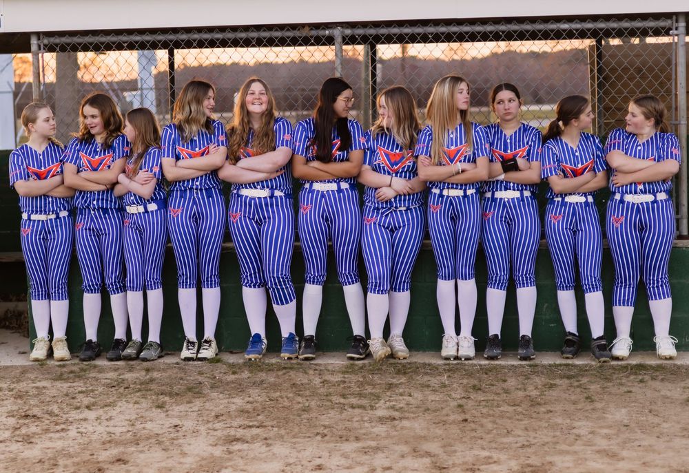 Team photo of softball players lined up in blue striped uniforms against fence.