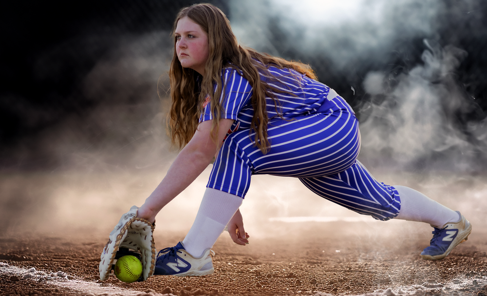 Softball player slides dramatically through dirt and smoke during game action.