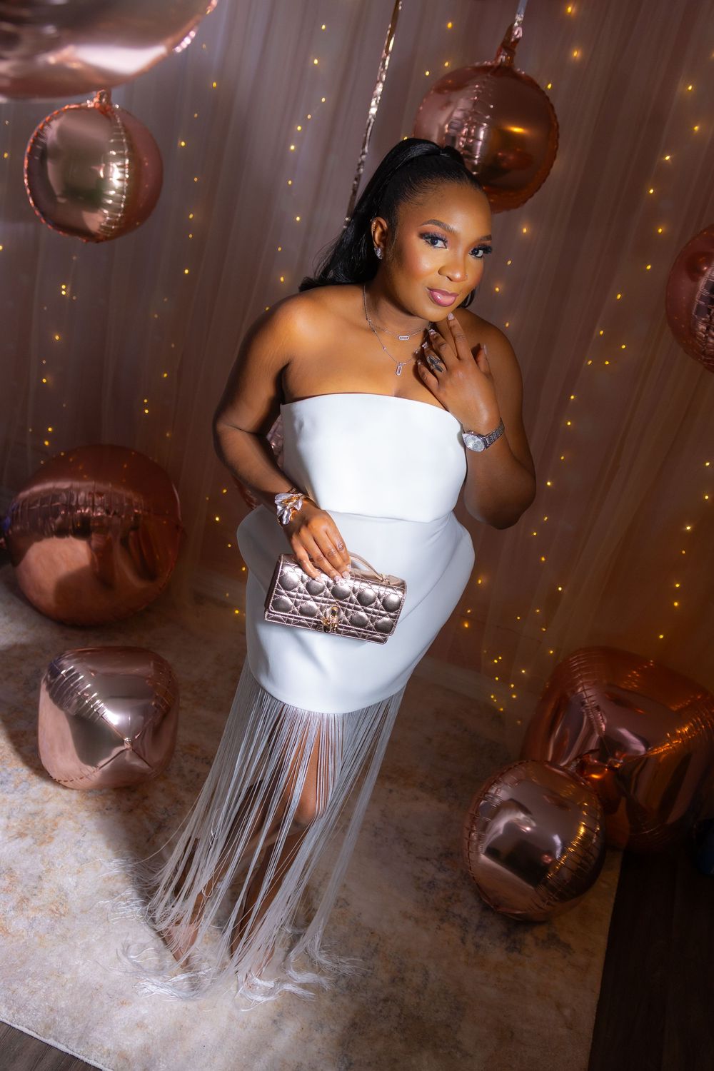 A glamorous party photoshoot featuring a white top and silver fringe skirt ensemble with sparkling decorative backdrop.
