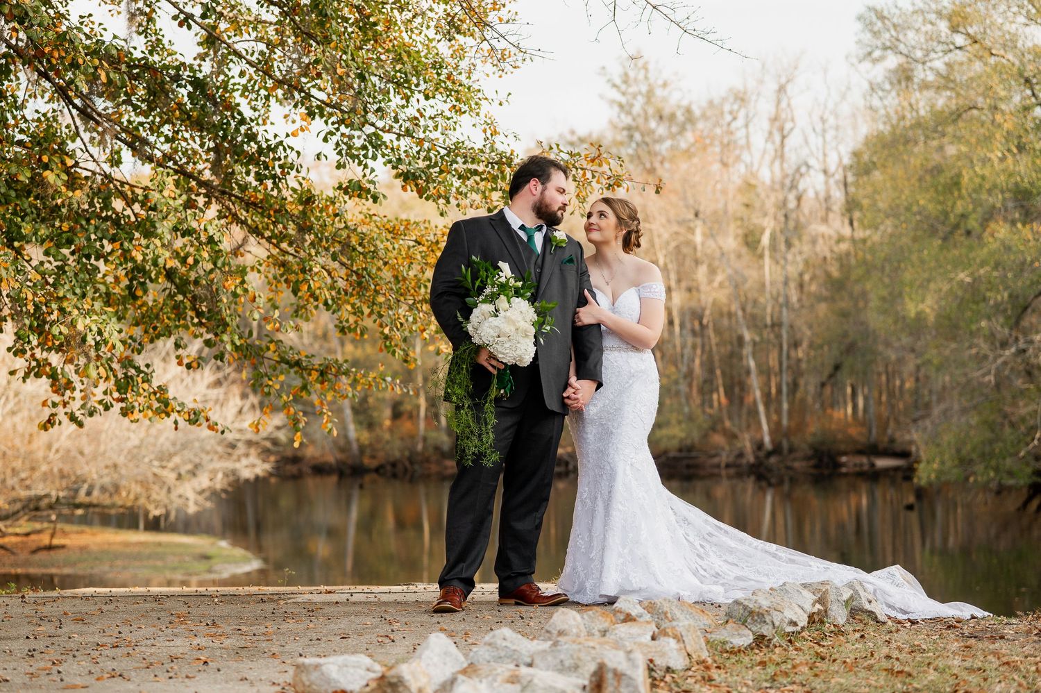 Scenic wedding photos by a tranquil pond surrounded by autumn trees.
