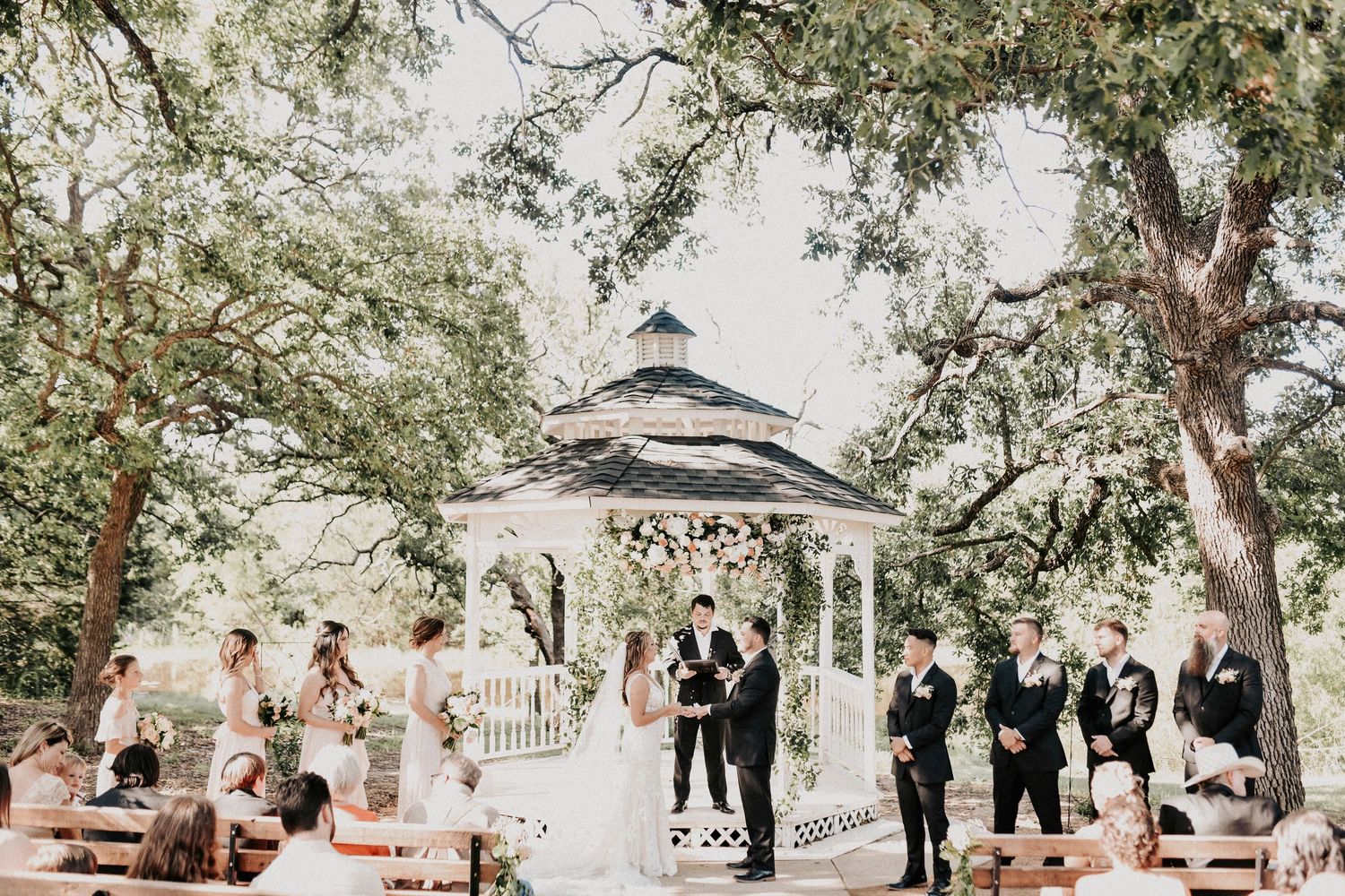 Bride and groom during their ceremony beneath towering oak trees at a romantic spring wedding in Texas.