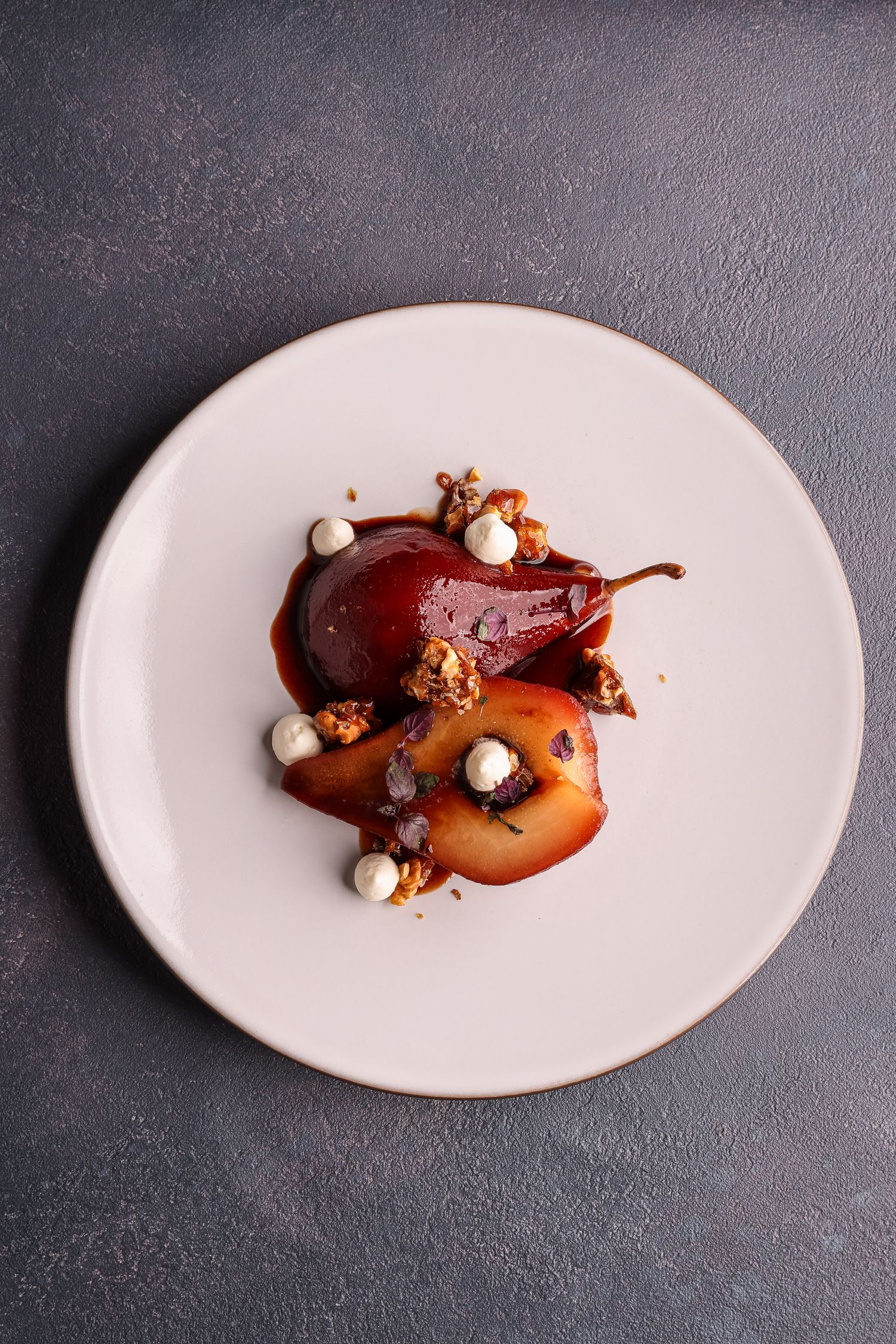 Elegant plated dessert featuring poached pears with chocolate sauce and small white meringue dots on a white oval plate.