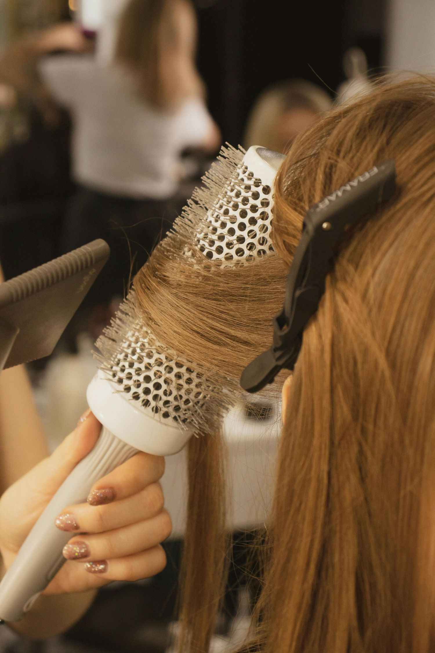 Hair stylist using a round brush to blow dry and style long brown hair during a professional salon treatment.