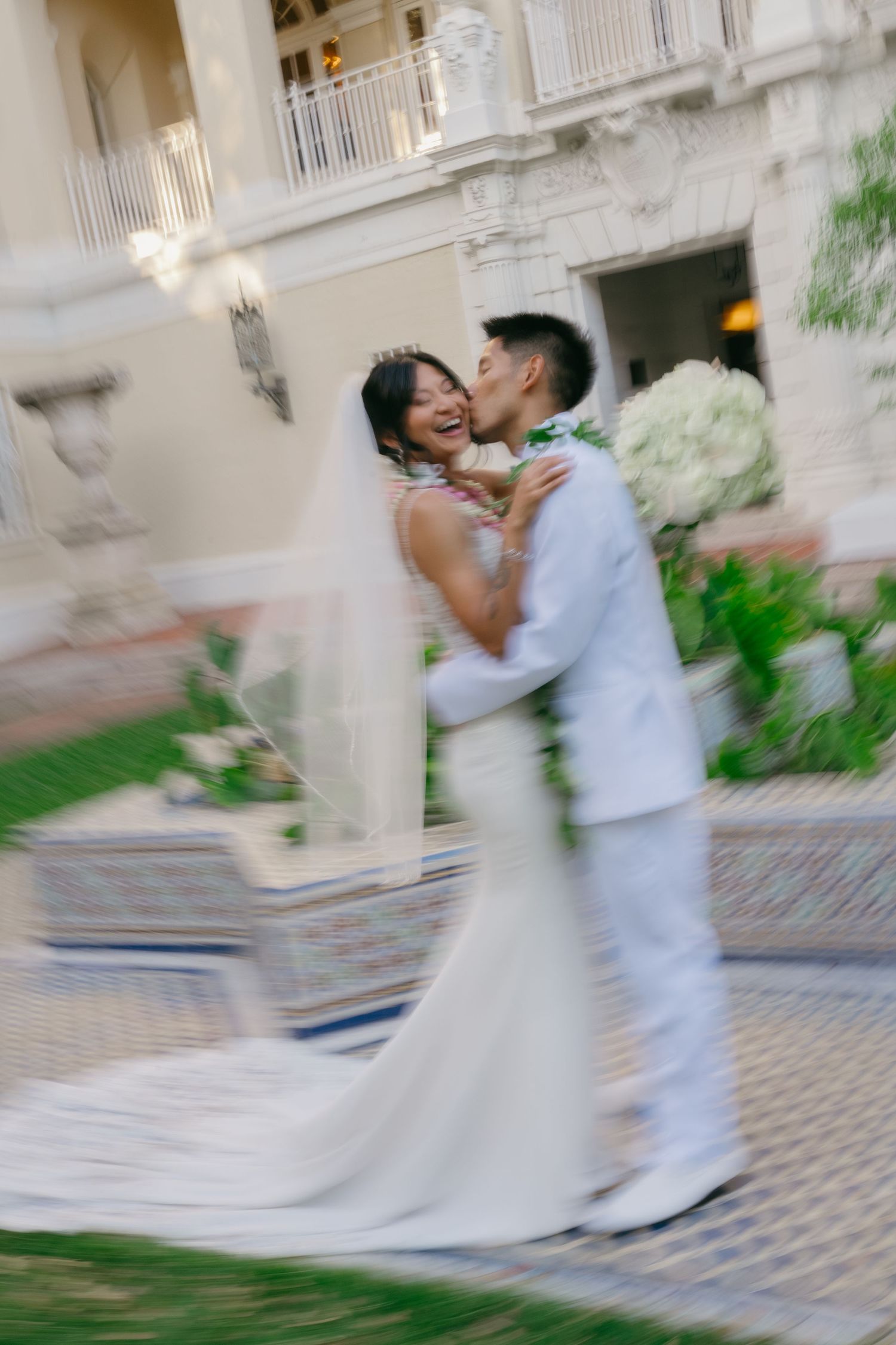 A couple in white wedding attire dances together in a romantic blur motion sequence on a stone courtyard.