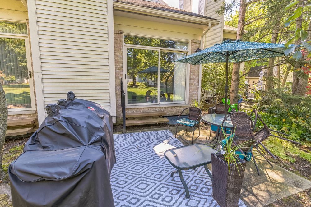 Cozy backyard patio with outdoor dining set, umbrella, grill, and sliding glass door to home.