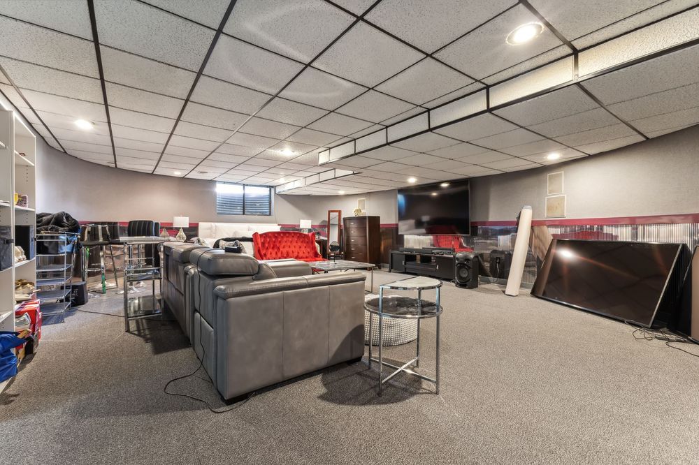 Spacious basement rec room with drop ceiling, gray carpet, and large sectional sofa.