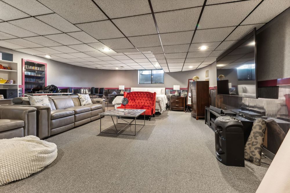 Large finished basement living area with drop ceiling, gray carpet, and mixed seating furniture.