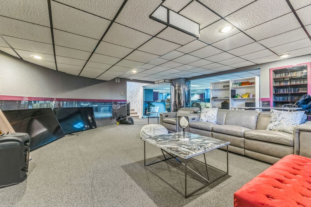 Spacious finished basement recreation room with drop ceiling, gray carpet, sectional sofa, and open shelving.