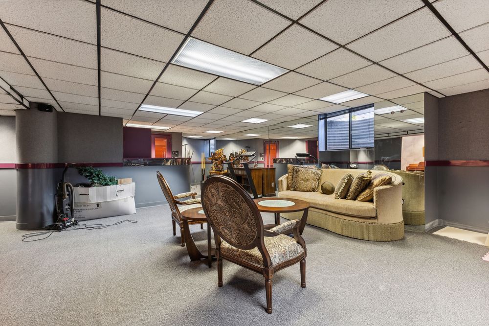 Expansive carpeted basement space with drop ceiling, seating area, and open floor plan layout.