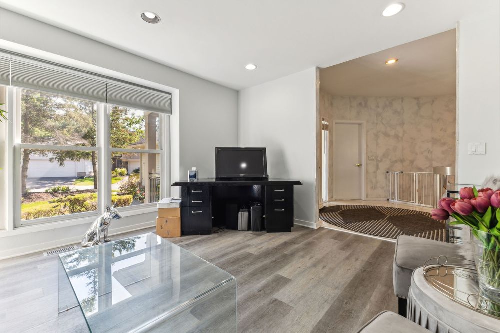 Bright living space with large windows, glass coffee table, hardwood floors, and garden views.